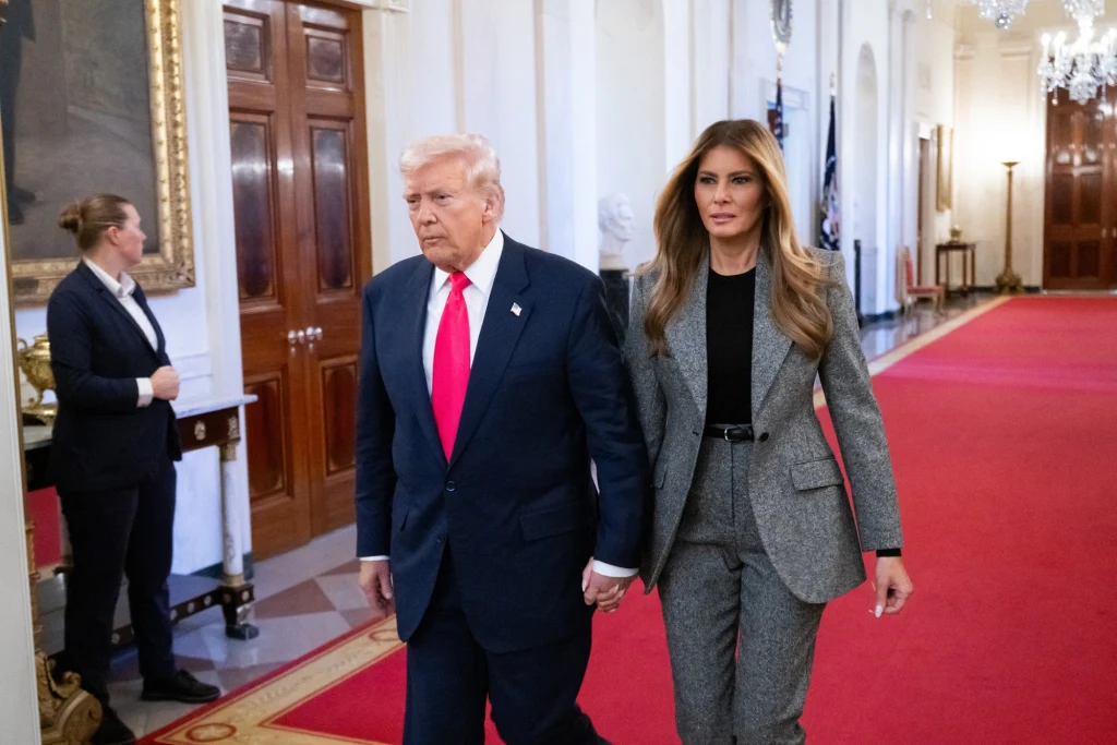 Majątek Donalda Trumpa kurczy się z powodu krachu na rynku kryptowalut Mężczyzna w garniturze i czerwoną krawatą oraz kobieta w szarym garniturze spacerują razem po eleganckim wnętrzu z czerwonym dywanem i żyrandolami. W tle widoczna osoba stojąca przy drzwiach.