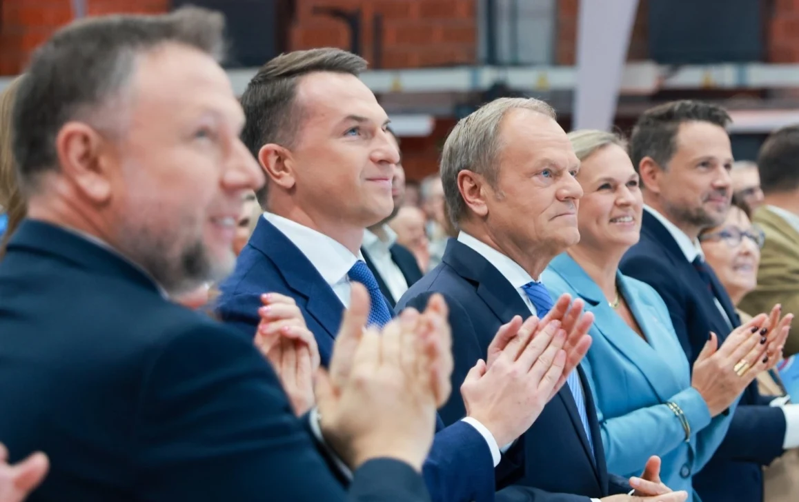 Politycy KO w trakcie październikowego kongresu partii Grupa elegancko ubranych osób stoi obok siebie, uśmiechnięci i oklaskują, zwracając uwagę na coś poza kadrem. W tle widoczne są elementy hali lub sali konferencyjnej.