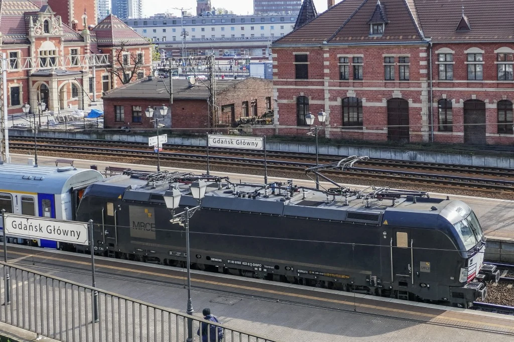 Fałszywy alarm na gdańskim Dworcu Głównym sprawił, że wstrzymano na kilka godzin ruch pociągów Czarny nowoczesny lokomotywa elektryczna stoi na peronie dworca Gdańsk Główny, otoczona zabytkowymi budynkami z cegły oraz tabliczkami informacyjnymi stacji.