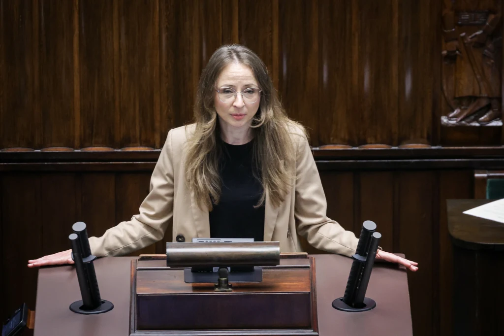 Trzecia wersja projektu reformy PIP - mimo wprowadzenia zmian - wciąż wzbudza duże kontrowersje Kobieta w okularach i marynarce stoi za mównicą w sali sejmowej, opierając ręce na pulpicie i patrząc przed siebie