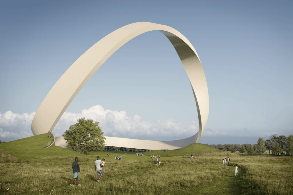 Wielka, nowoczesna instalacja w kształcie obłego pierścienia ustawiona na zielonym wzgórzu, wokół której spacerują ludzie, dzieci bawią się na trawie, a na niebie widać kilka obłoków.