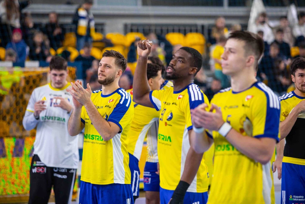 Industria Kielce Zawodnicy drużyny piłki ręcznej w żółto-niebieskich strojach gratulują sobie na boisku po zakończonym meczu, w tle widownia oraz bramkarz w białej koszulce.