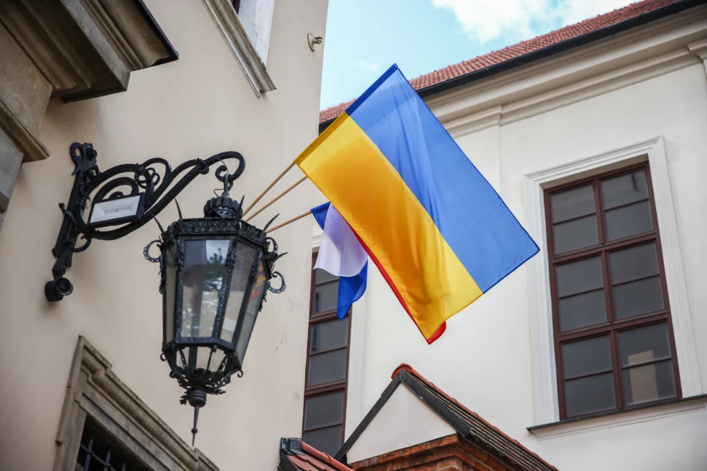 Ukraińcy kupują coraz więcej online Flaga Ukrainy powiewająca na wietrze na tle zabytkowego budynku. W tle również widoczna flaga Polski oraz stara uliczna latarnia przyścienna.