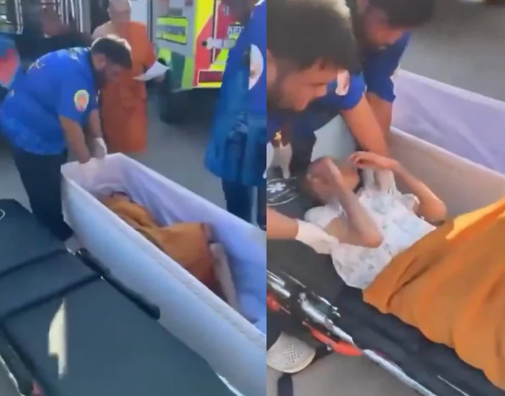 Szok w świątyni pod Bangkokiem. Kobieta "ożyła" chwilę przed kremacją Ratownicy udzielają pomocy osobie leżącej w trumnie, ubrane w szpitalną koszulę, przykrytej pomarańczowym materiałem, wokół stoją sanitariusze w niebieskich mundurach oraz widoczna jest karetka pogotowia.