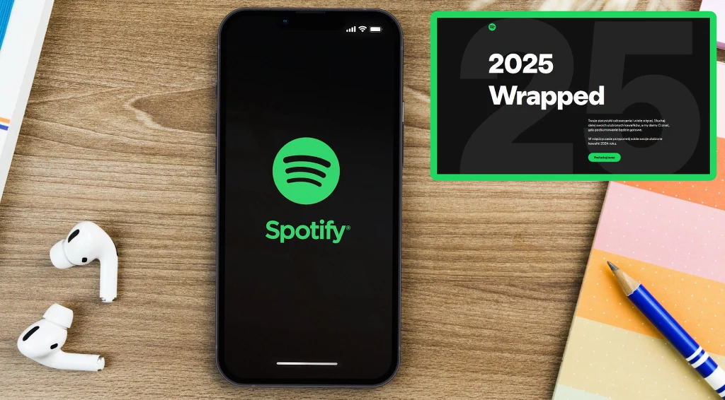 Kiedy zacznie się Spotify Wrapped 2025? Wyczekiwane podsumowanie roku już coraz bliżej Czarny smartfon z uruchomioną aplikacją Spotify leży na drewnianym biurku, obok białych bezprzewodowych słuchawek i niebiesko-żółtego długopisu. W prawym górnym rogu widnieje grafika z napisem 2025 Wrapped.