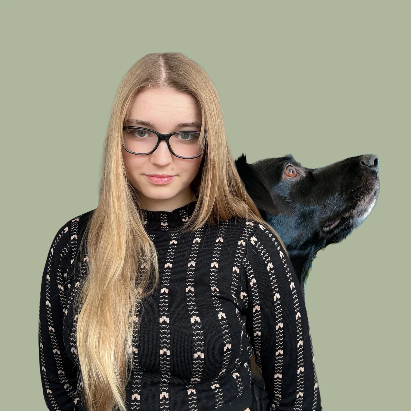 Młoda kobieta z długimi blond włosami, ubrana w czarną bluzkę z wzorem, stoi obok dużego czarnego psa, którego pysk skierowany jest w bok na zielonym, jednolitym tle.
