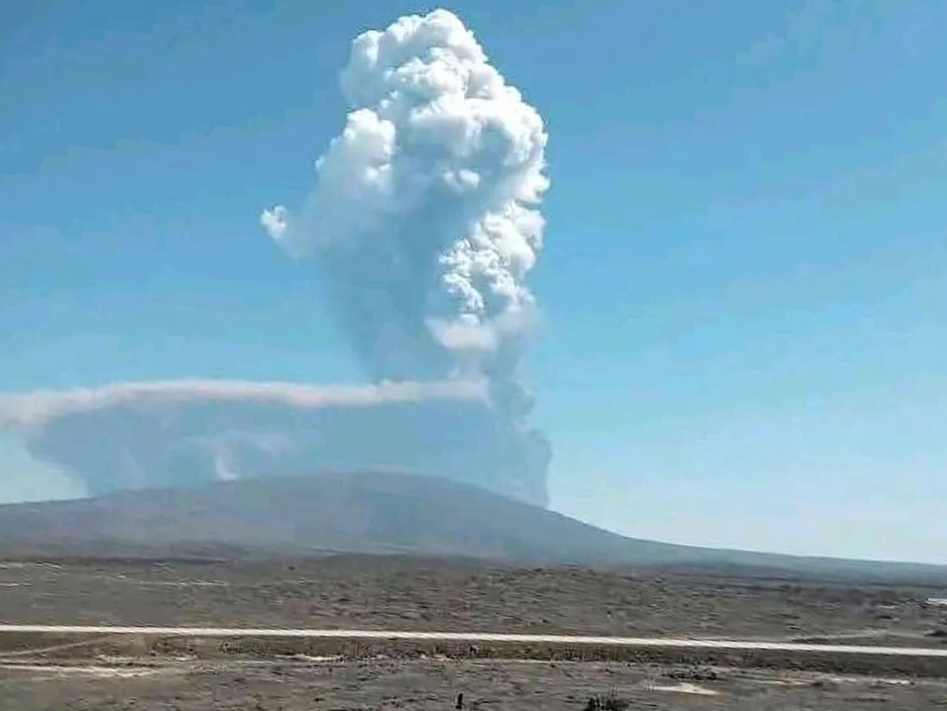 Potężny wybuch wulkanu Hayli Gubbi. Popiół wzbił się na 15 km Erupcja wulkanu z wysoką kolumną dymu i popiołu unoszącą się nad ciemnym, suchym terenem w jasny, bezchmurny dzień.