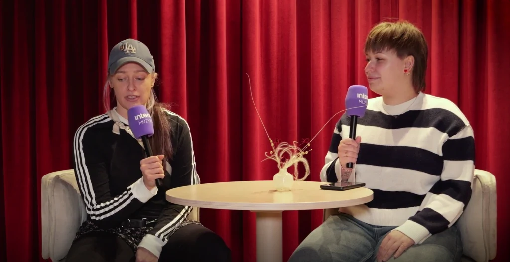 Matylda Damięcka stworzyła autorską narrację do filmu "Rejs" Dwie kobiety siedzące przy okrągłym stoliku na jasnych fotelach, trzymają mikrofony z logo stacji, za nimi czerwona kotara, na stole biała dekoracja.