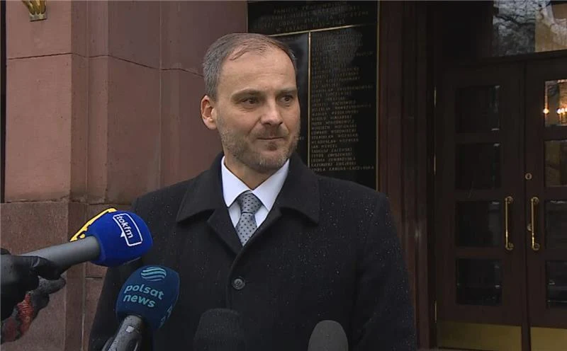 Rzecznik polskiego MSZ Maciej Wewiór wypowiedział się na temat spotkania z ambasadorem Izraela w Polsce Mężczyzna w garniturze i płaszczu stoi przed wejściem do budynku, wokół niego ustawione są mikrofony różnych stacji telewizyjnych, m.in. Polsat News, udzielając prawdopodobnie wywiadu lub wygłaszając oświadczenie.