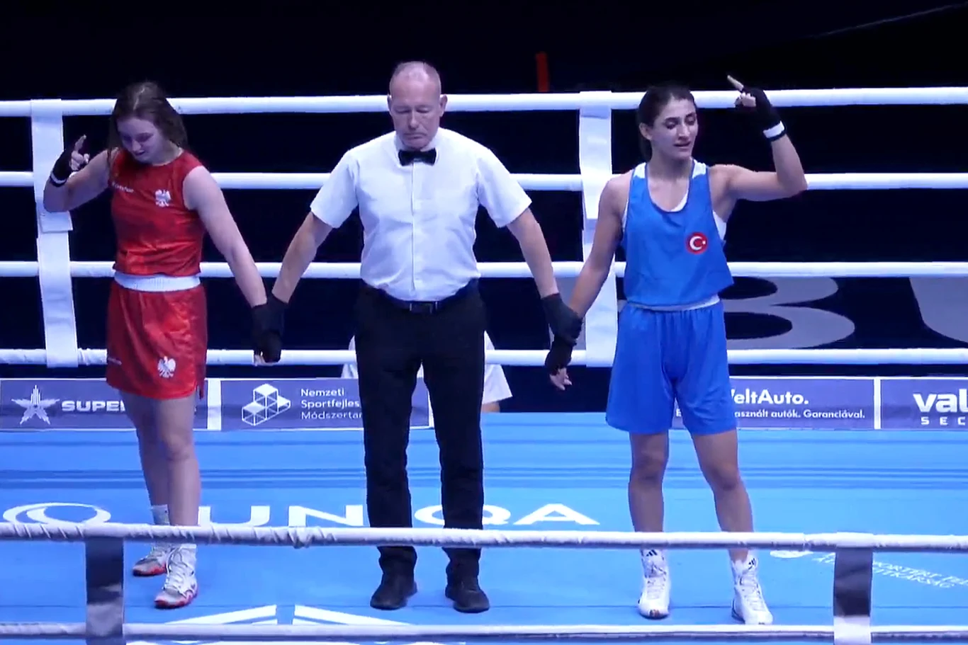 Julia Szeremeta i Benek Pinar w oczekiwaniu na werdykt Dwie zawodniczki boksu stoją w ringu wraz z sędzią. Jedna z nich, ubrana w niebieski strój z turecką flagą, trzyma uniesioną rękę w geście zwycięstwa, podczas gdy druga, ubrana na czerwono, pochyla głowę.