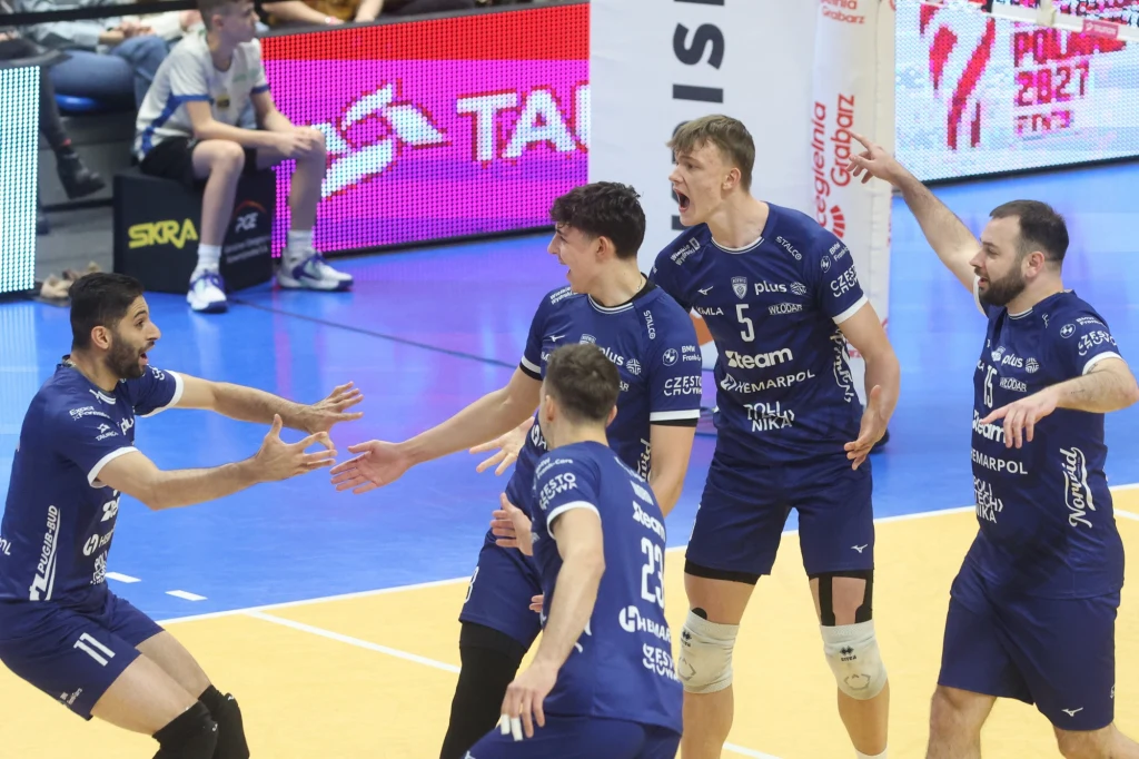 Siatkarze klubu z Częstochowy, w środku Jakub Nowak Grupa siatkarzy w niebieskich strojach świętuje zdobyty punkt na hali sportowej. Zawodnicy mają wyraźnie zadowolone miny, dwóch z nich jest wyraźnie podekscytowanych, a wszyscy są w dynamicznych pozach.