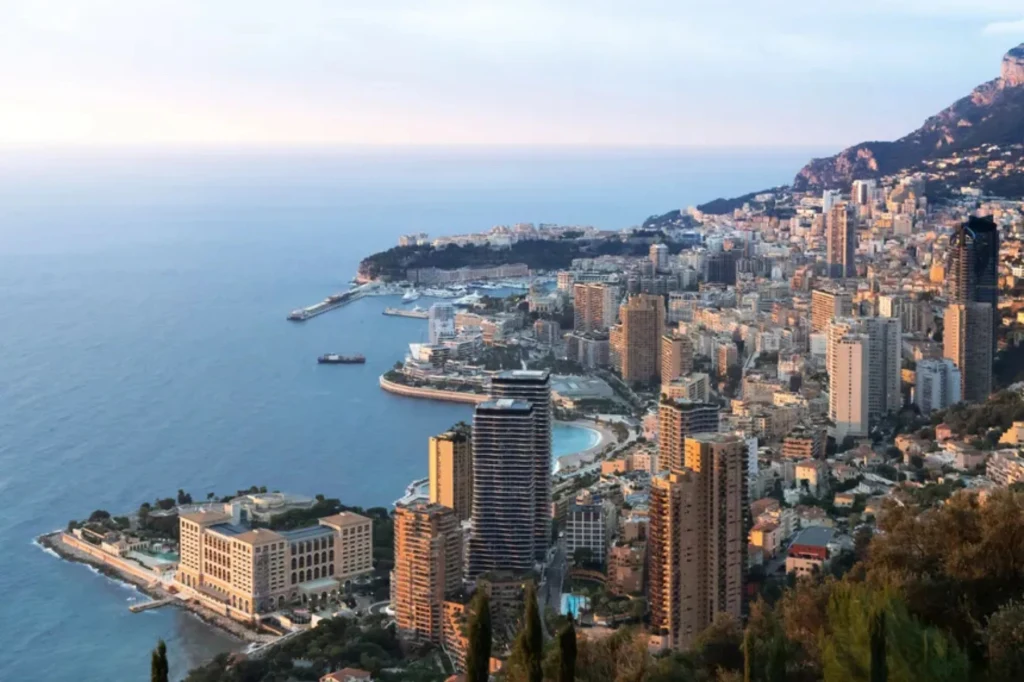 Panorama nadmorskiego miasta z przeważającymi wysokimi budynkami, malowniczym wybrzeżem i otaczającymi wzgórzami. Widoczne są zatoki, port oraz luksusowe apartamentowce położone w pobliżu turkusowego morza.