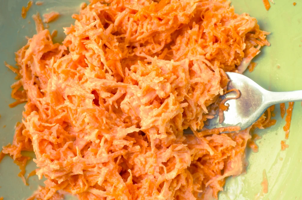 Łatwa surówka do obiadu? Oto przepis na marchew z chrzanem Starte marchewki wymieszane z kremowym sosem, widoczne na tle jasnej miski z metalowym widelcem.