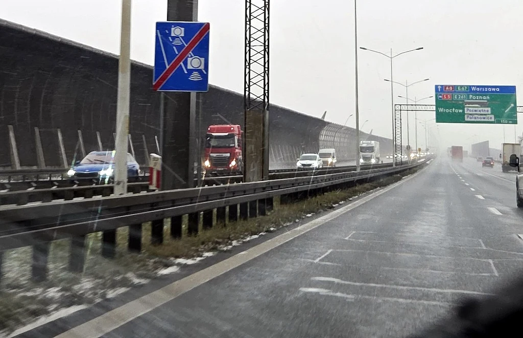 Odcinkowy pomiar prędkości na A8 (autostradowa obwodnica Wrocławia) już działa Widok na autostradę z barierą dźwiękochłonną po lewej stronie oraz tablicami informacyjnymi i znakami drogowymi. Samochody jadą w jednym kierunku, a droga w przeciwnym jest pusta. Znaki informują m.in. o zakazie zatrzymywania się i obecności fotoradaru.