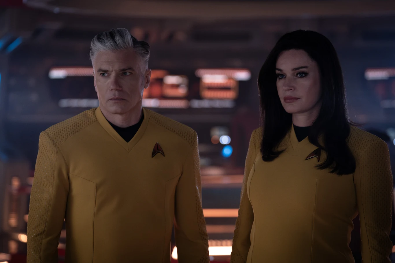 Fani będą mogli też ponownie wyruszyć w podróż na U.S.S. Enterprise w ramach czwartego sezonu Star Trek: Strange New Worlds (Star Trek: Nieznane nowe światy). Dwoje ludzi w żółtych mundurach science fiction stoi obok siebie na futurystycznym mostku statku kosmicznego, patrząc w jednym kierunku, za ich plecami rozmyte światła konsoli i ekrany elektroniczne.