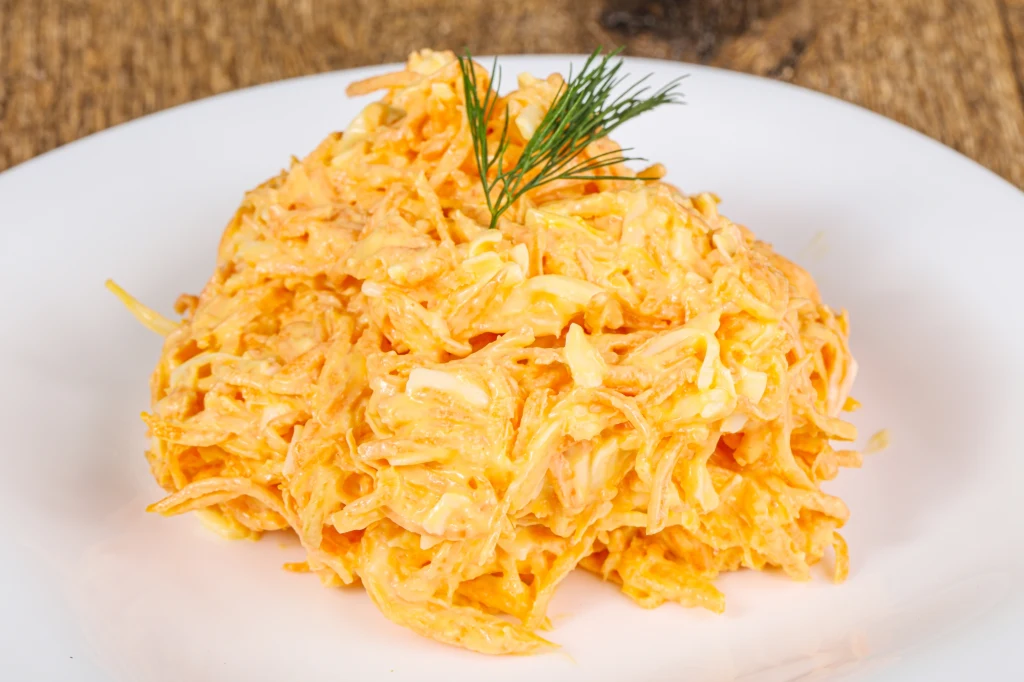Marchew z chrzanem jest idealna na jesień i zimę Tarta marchewka wymieszana z majonezem i jajkiem, podana w formie kopczyka na białym talerzu, udekorowana gałązką świeżego koperku.