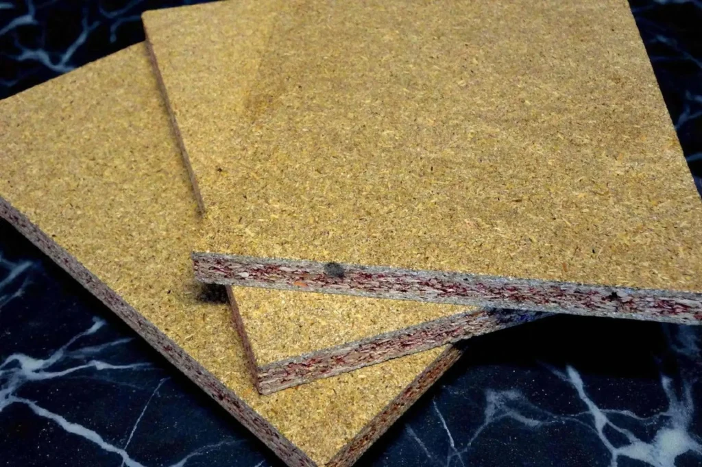 Trzy płyty wiórowe ułożone na sobie, z wyraźnie widoczną strukturą warstw i przekrojem, leżące na czarnym blacie przypominającym marmur.