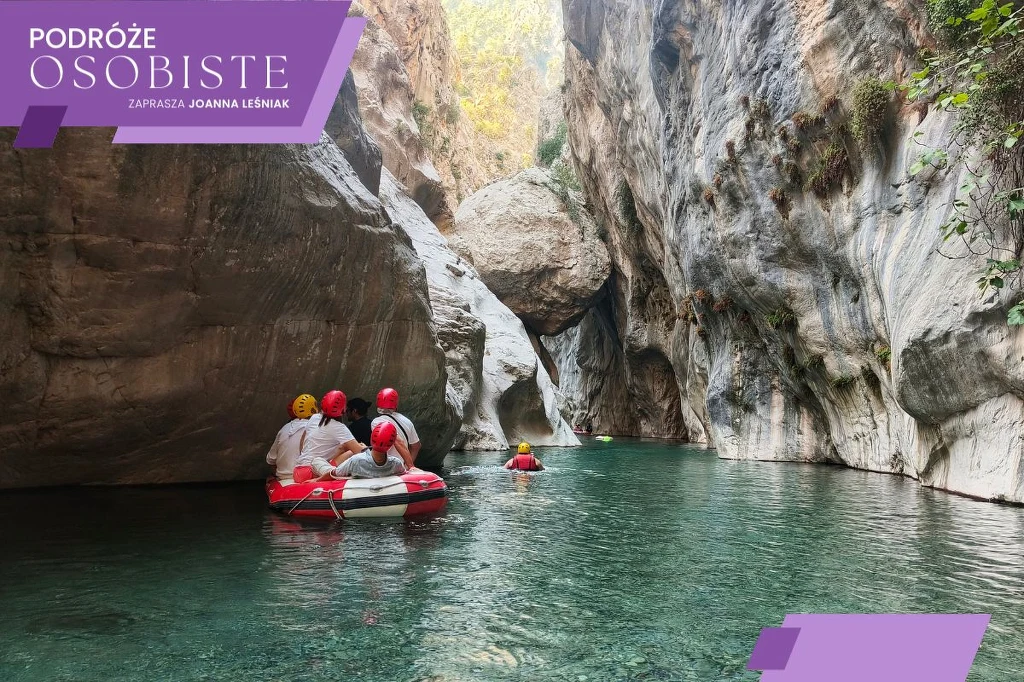 Grupa osób w kaskach i kamizelkach ratunkowych płynąca pontonem po wąskim, skalistym kanionie z przejrzystą wodą, otoczenie pełne wysokich skał i delikatnej roślinności.
