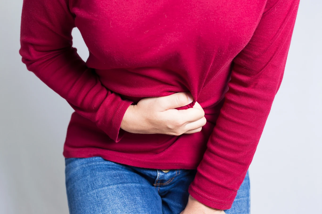 Diagnostyka endometriozy często trwa latami Osoba w czerwonej bluzce i dżinsach trzymająca się za brzuch, wyrażająca ból lub dyskomfort.