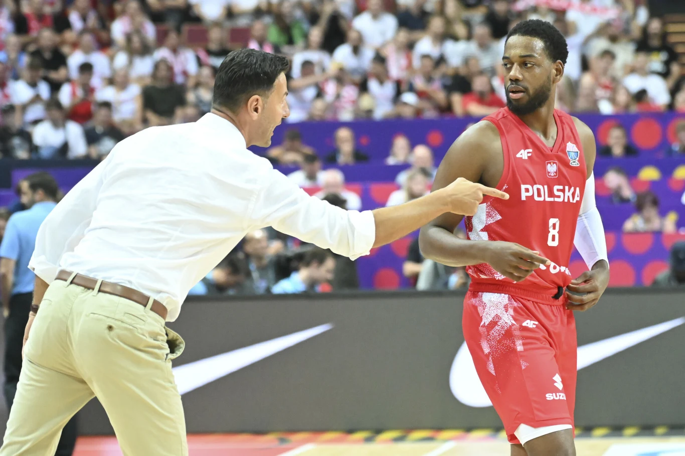 Igor Milicić w najbliższych meczach reprezentacji bedzie musiał radzić sobie bez Jordana Loyda Trener w białej koszuli energicznie udziela wskazówek zawodnikowi reprezentacji Polski w czerwonym stroju z numerem 8 podczas meczu koszykówki w hali pełnej kibiców.
