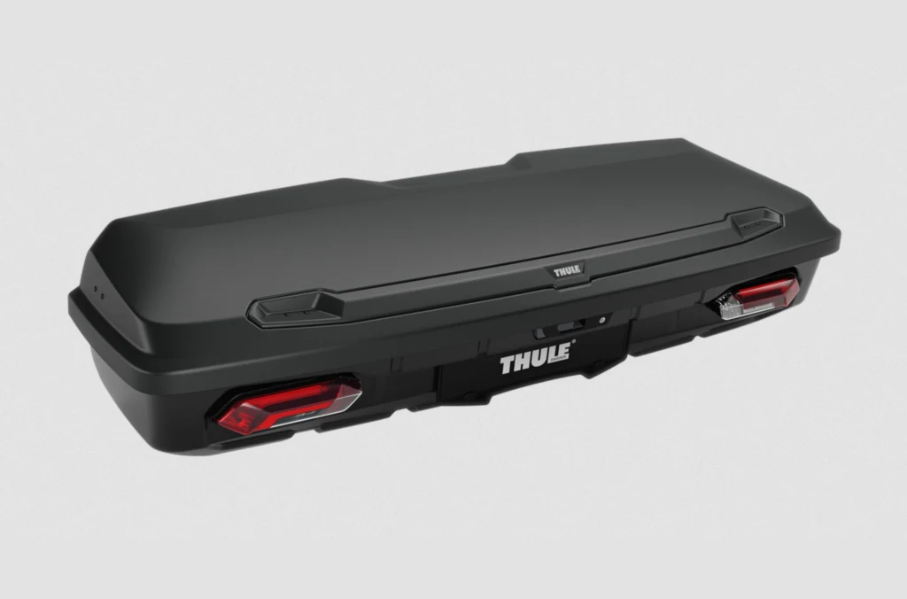 Czarny bagażnik samochodowy marki Thule o aerodynamicznym kształcie, wyposażony w tylne światła odblaskowe i logo producenta umieszczone centralnie na przodzie.