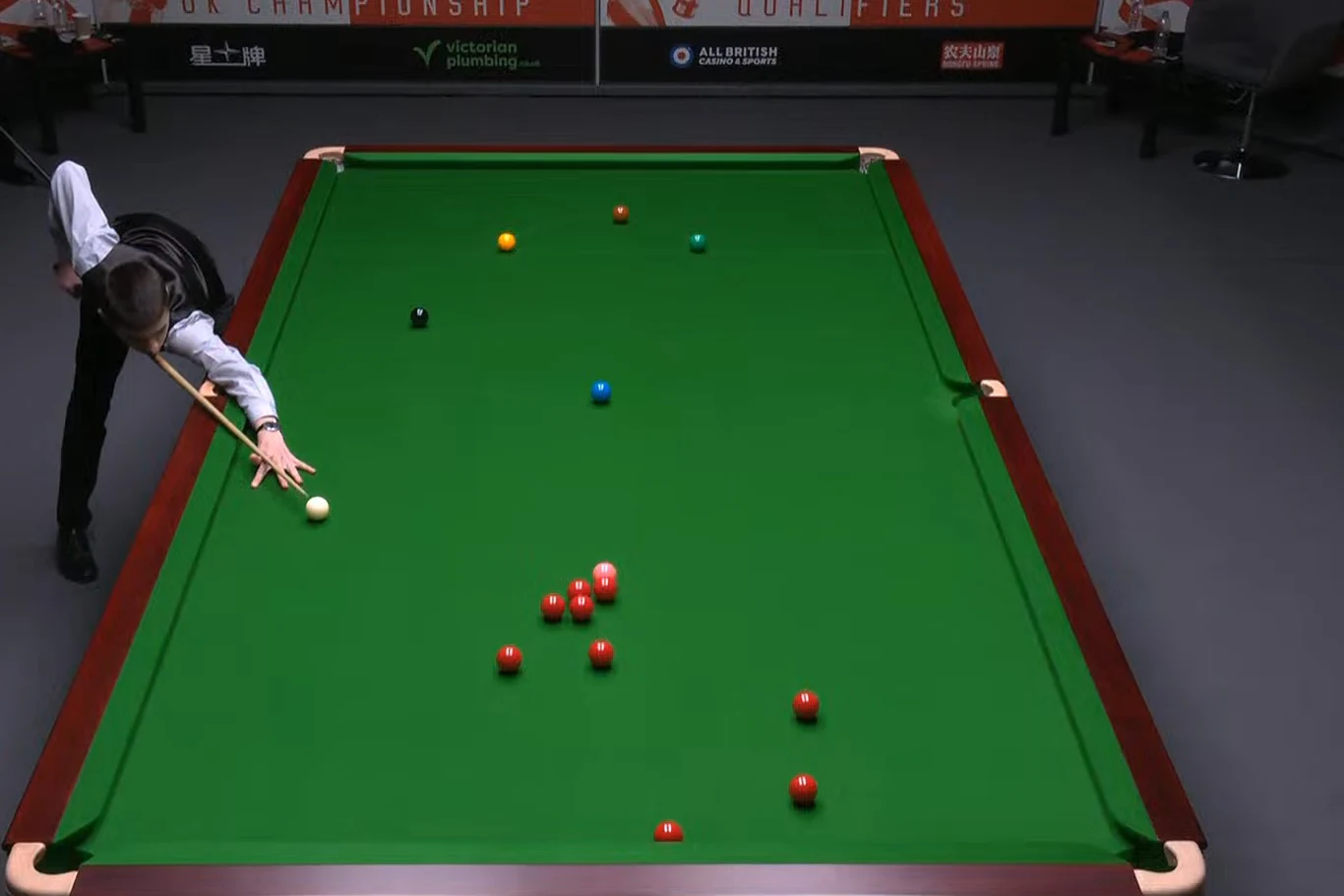 Michał Szubarczyk Zawodnik w eleganckiej kamizelce wykonuje uderzenie na stole bilardowym w trakcie meczu snookera, wokół grupy czerwonych bil rozmieszczonych na zielonym suknie.