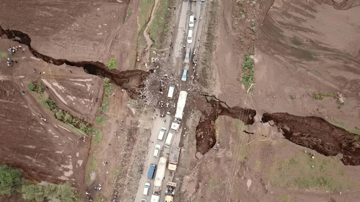 Afryka się rozpada. Pęknięcie cały czas rośnie Droga przecięta głębokimi rozpadlinami ziemi, utrudniająca ruch pojazdów. Samochody stoją w korku po obu stronach rozpadliny. Wokół widać skarpę i osuwisko, teren pokryty brunatną ziemią.