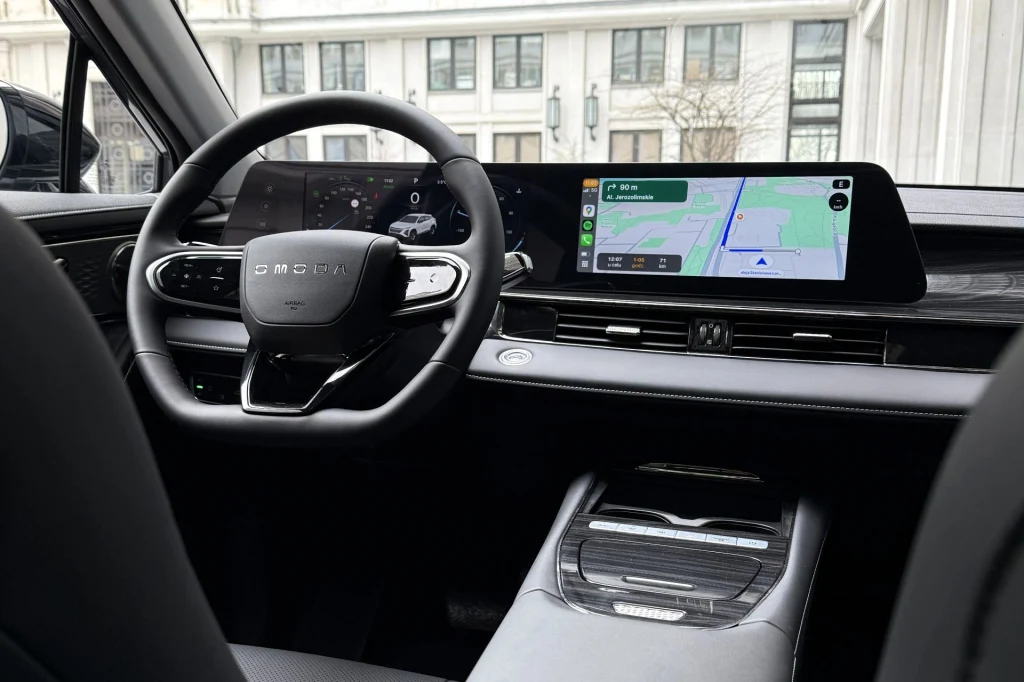 Nowoczesny kokpit samochodu z cyfrowym wyświetlaczem przed kierowcą oraz dużym ekranem multimedialnym prezentującym mapę nawigacyjną, otoczony eleganckimi, czarnymi wykończeniami wnętrza.