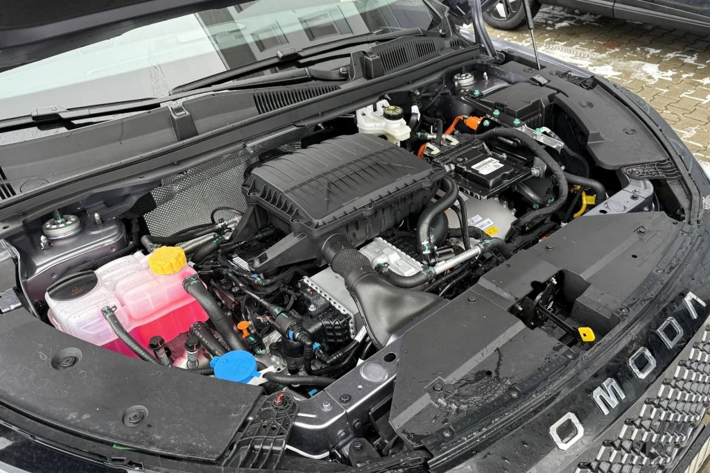 Komora silnika nowoczesnego samochodu marki Omoda z widocznymi elementami technicznymi, zbiornikiem płynu chłodniczego oraz rurami i przewodami.