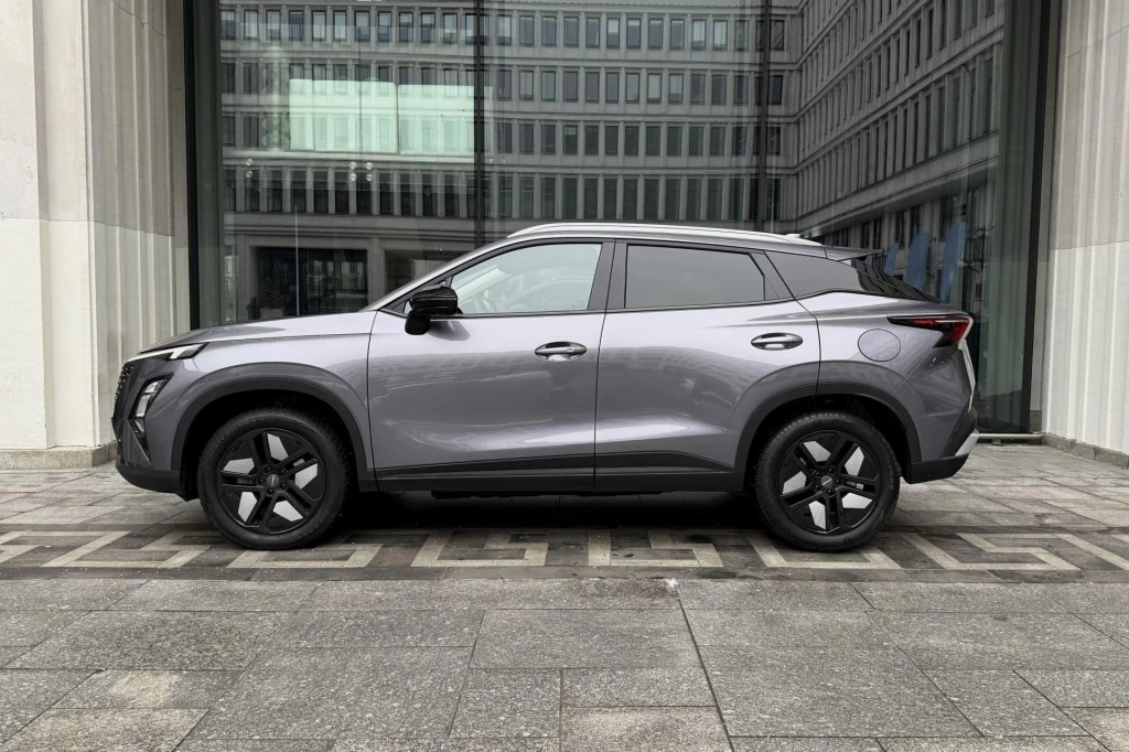 Srebrny SUV nowoczesnego designu zaparkowany na tle dużych przeszklonych okien budynku biurowego z betonową nawierzchnią i geometryczną ścieżką chodnikową.