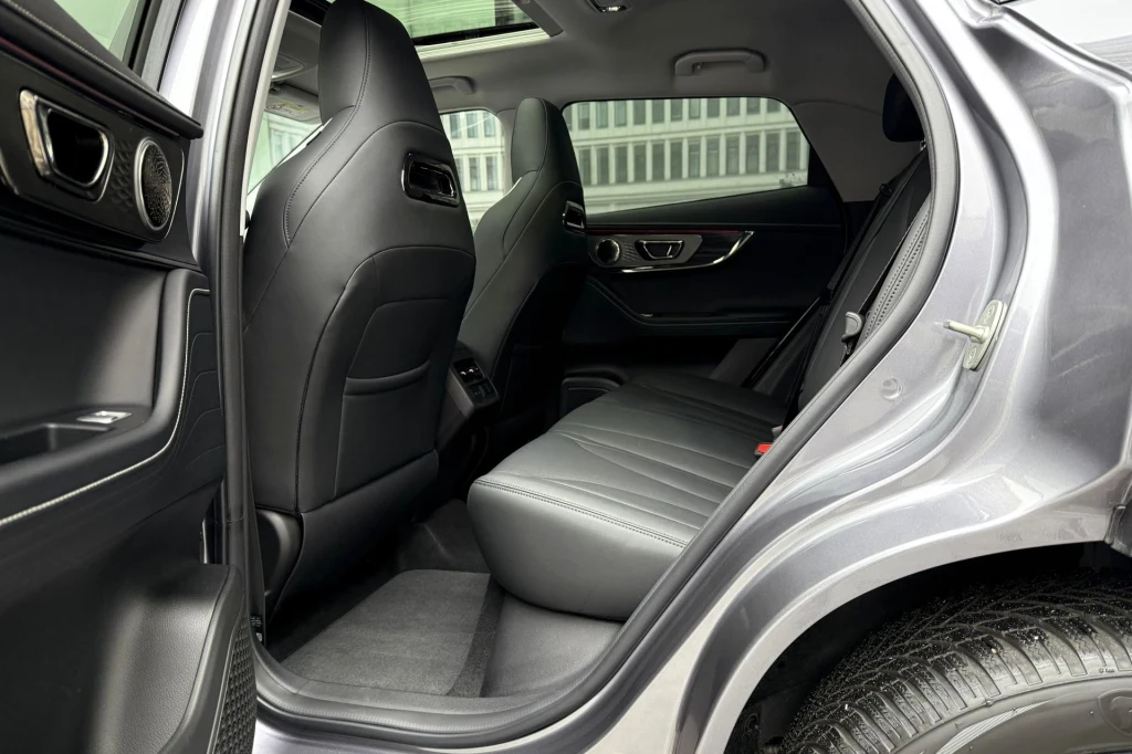 Widok na tylne fotele luksusowego samochodu osobowego z otwartymi drzwiami, elegancka skórzana tapicerka, czyste wnętrze oraz fragment opony samochodu.