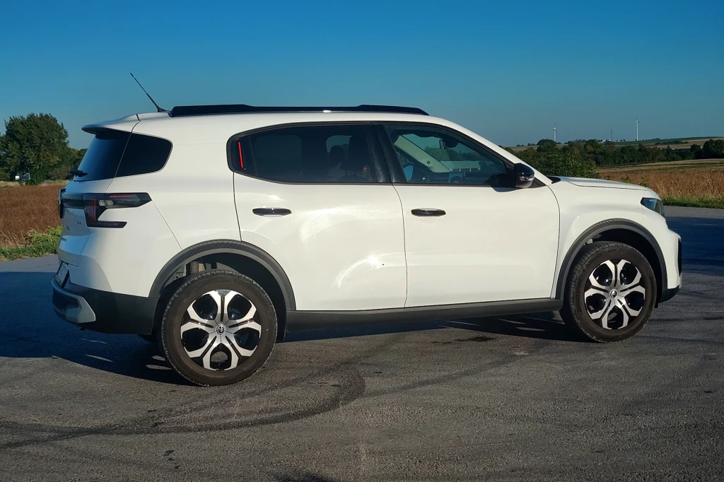 Citroen C3 Aircross to samochód komfortowy. Sportowych wrażeń w nim nie znajdziemy Biały samochód typu SUV zaparkowany na pustym placu asfaltowym, w tle widoczne pola i linia drzew, niebo bezchmurne.