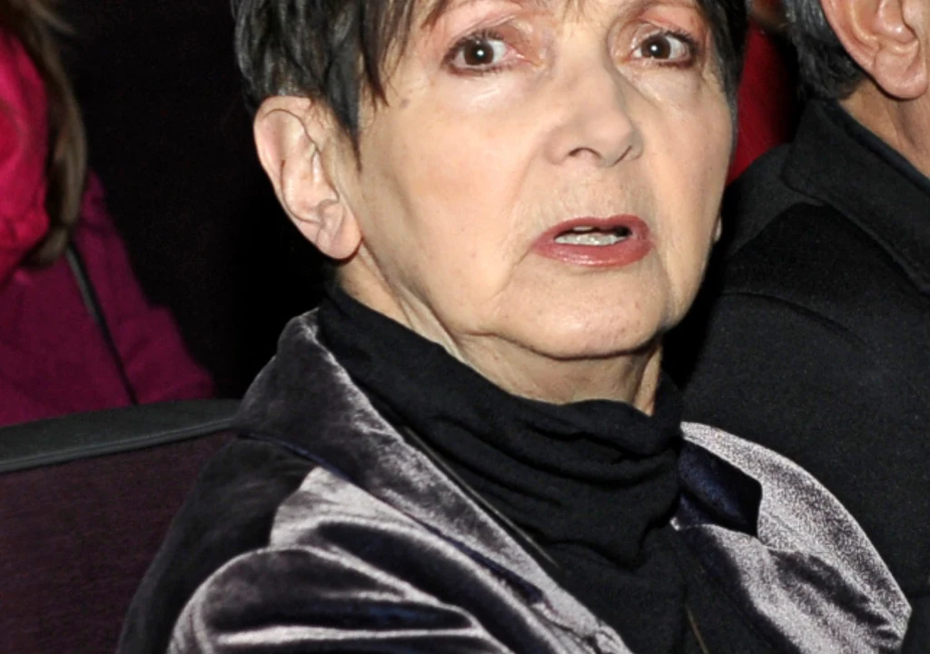 Halina Kunicka Starsza kobieta o krótkich, ciemnych włosach ubrana w aksamitną marynarkę i czarny golf siedzi na tle innych osób, patrząc prosto w stronę aparatu.