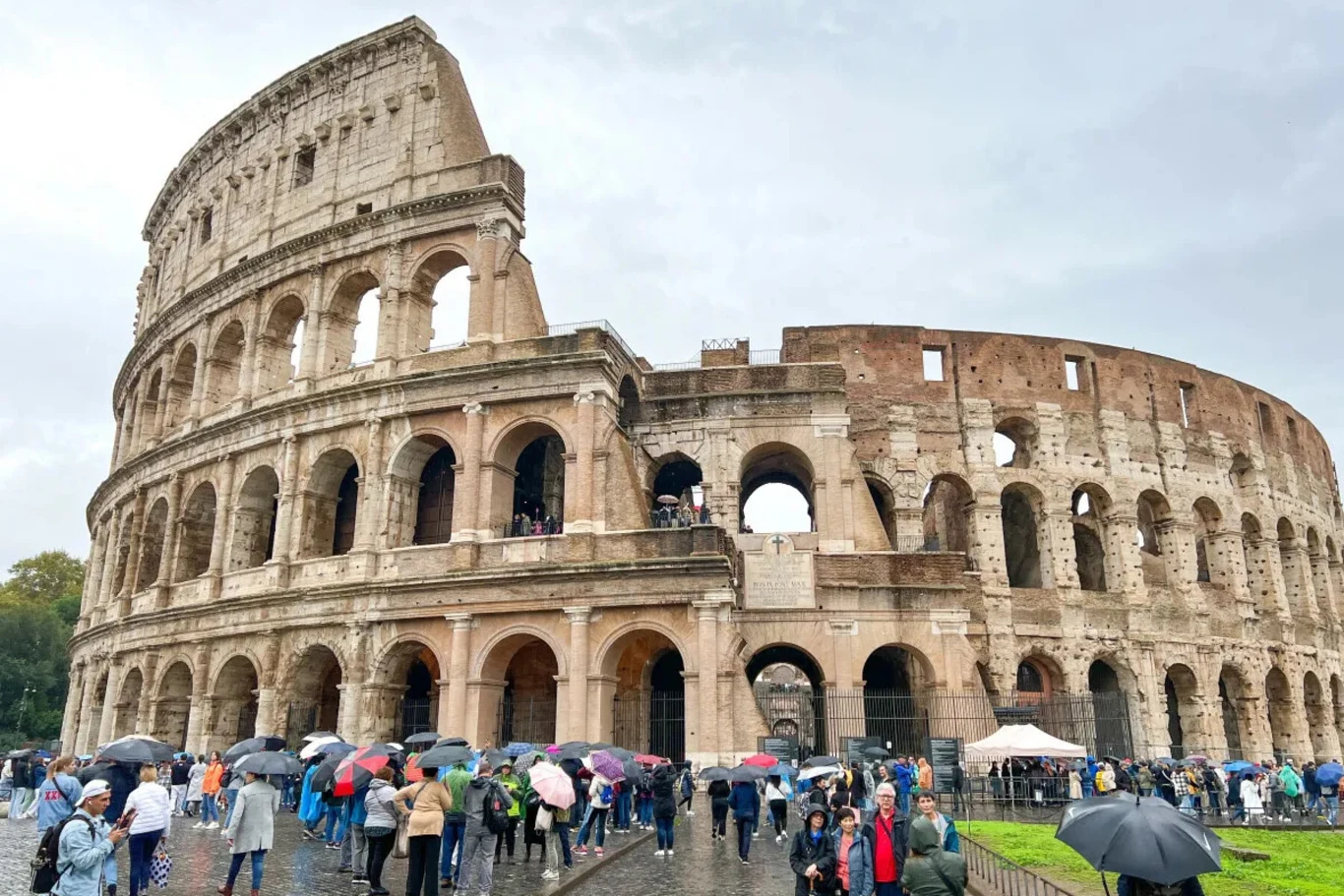 Niedaleko słynnego Koloseum zakonnica wcieliła się w policjantkę, aby rozładować korek Koloseum w Rzymie otoczone przez liczną grupę turystów, z których wielu trzyma parasole. Rzymski amfiteatr dominuje w kadrze, a na pierwszym planie widać ludzi spacerujących wokół zabytku.