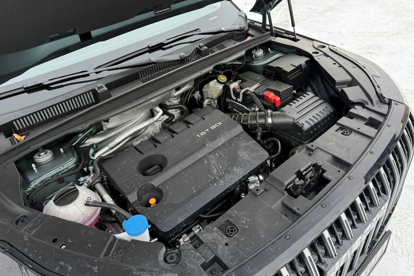 Komora silnika samochodu z widocznym nowoczesnym silnikiem spalinowym, akumulatorem, zbiornikiem płynu chłodniczego oraz elementami instalacji elektrycznej i mechanicznej.