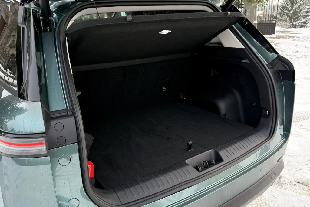Otwarty bagażnik samochodu terenowego z dużą, przestronną przestrzenią ładunkową. Wnętrze bagażnika jest czyste i uporządkowane, wokół widoczny śnieg i fragment ogrodzenia.
