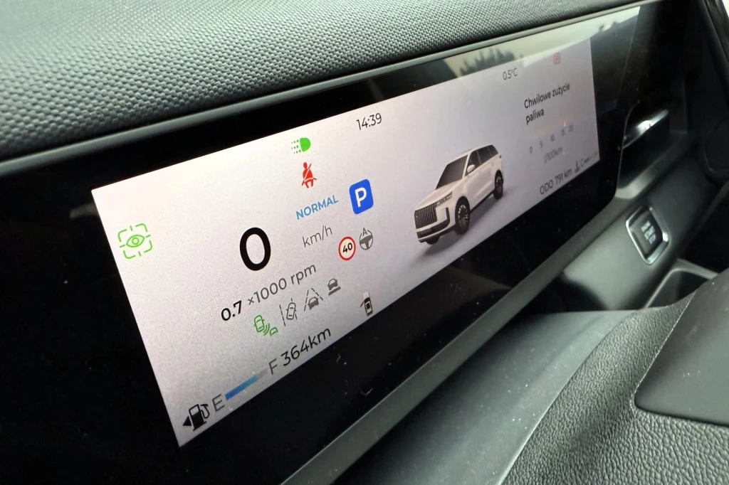 Nowoczesny cyfrowy kokpit samochodu z dużym ekranem prezentującym szczegółowe informacje o pojeździe, takie jak prędkość, poziom paliwa, zasięg, tryb jazdy oraz wizualizację samochodu.