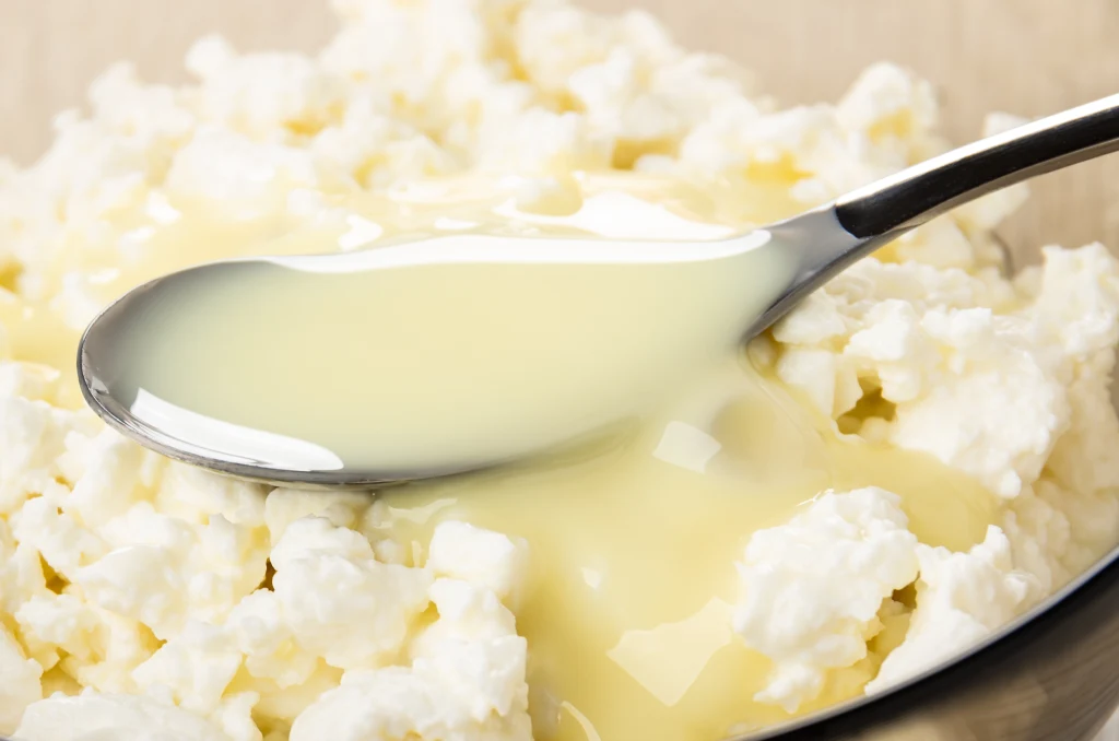 Twaróg można jeść na setki sposobów: na słodko i wytrawnie Łyżka nabiera białego twarogu skąpanego w gęstym żółtawym płynie, prawdopodobnie śmietanie lub mleku skondensowanym, zbliżenie ukazujące konsystencję obu składników.