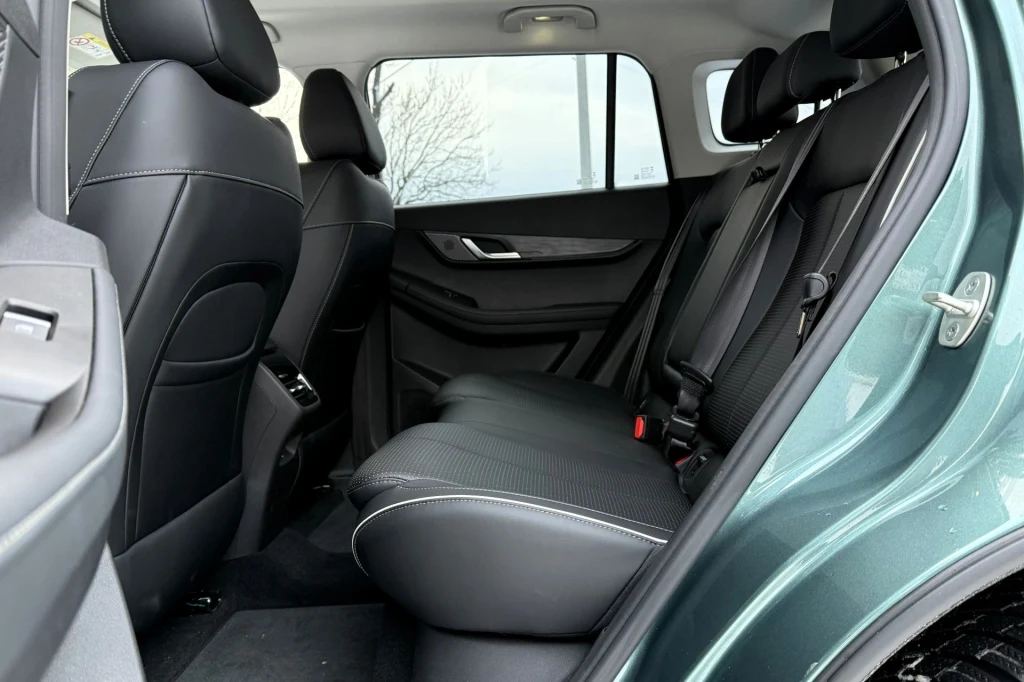 Tylne siedzenia nowoczesnego samochodu osobowego, widoczne wysokiej jakości tapicerki, czarne fotele z przeszyciami, przestronne wnętrze oraz minimalne elementy wyposażenia.