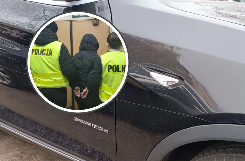 Dwóch wandali, 19 uszkodzonych aut. Policja w akcji na dwóch osiedlach. Dwóch funkcjonariuszy policji w żółtych kamizelkach odblaskowych prowadzi osobę w ciemnej kurtce z kajdankami na rękach, obok fragment czarnego samochodu policyjnego.