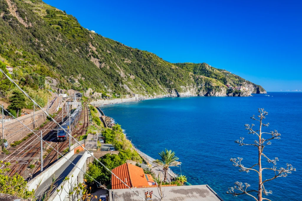 Cinque Terre Express to jedna z największych atrakcji Włoch. Pociąg oferuje niezapomniane widoki na wybrzeże i wzgórza i łączy urokliwe miasteczka Turkusowa woda morza kontrastuje z zielonymi, stromymi wzgórzami wybrzeża. Przez dolną część krajobrazu biegną tory kolejowe, wzdłuż których przejeżdża pociąg. W pobliżu rosną palmy i agawa, dachy zabudowań pokryte są pomarańczową dachówką.