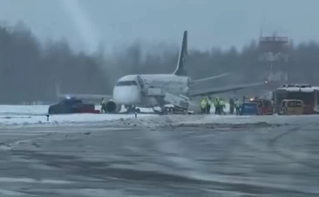 Samolot PLL LOT wypadł z pasa startowego na lotnisku w Wilnie Samolot pasażerski znajduje się na zaśnieżonym pasie startowym, wokół niego zgromadzone są służby ratownicze i pojazdy techniczne. W tle widoczny jest las i infrastruktura lotniska, panuje zimowa aura.