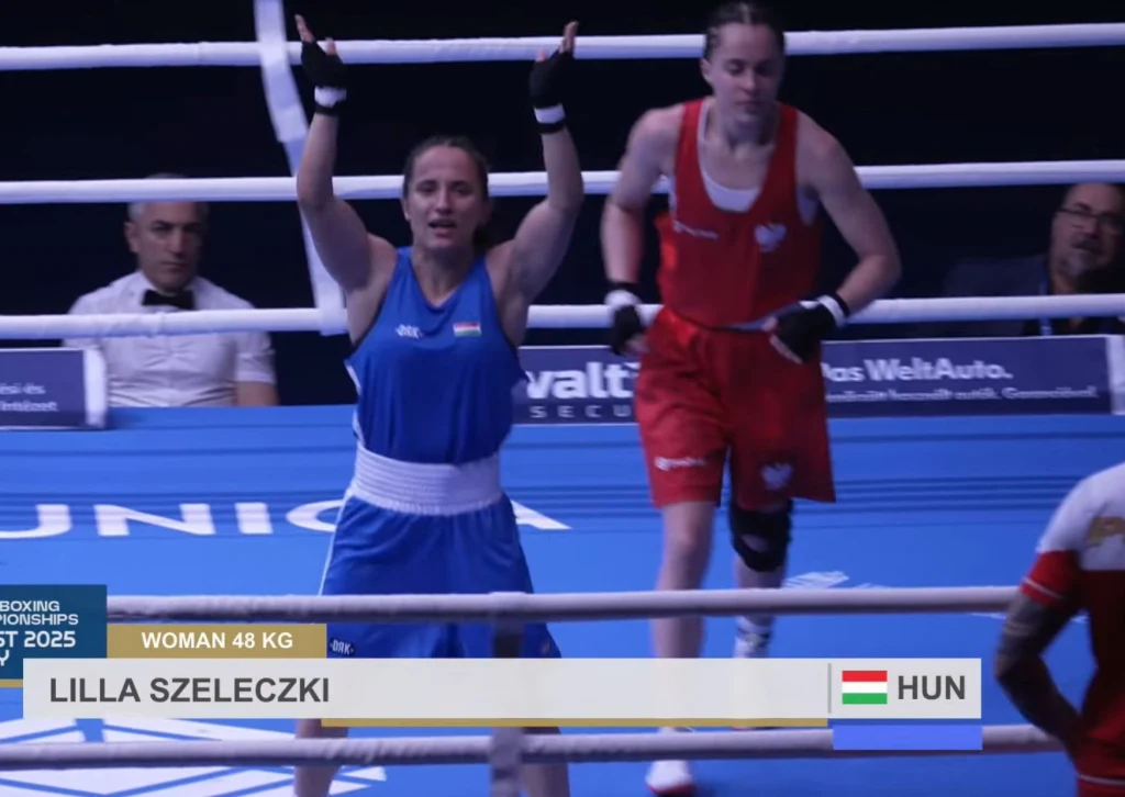 Dwóch zawodniczek w ringu bokserskim podczas walki w kategorii 48 kg, jedna cieszy się po zakończeniu pojedynku, druga opuszcza ring. Widoczna tablica z nazwiskiem zwyciężczyni oraz flagą Węgier.