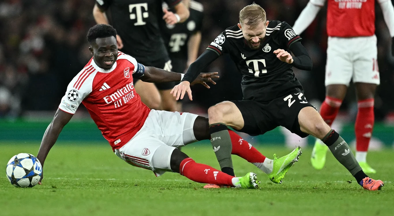 Bukayo Saka kontra Konrad Laimer. W Londynie doszło do wymiany ciosów Dwóch piłkarzy walczy o piłkę podczas meczu, zawodnik w czerwono-białej koszulce wykonuje wślizg, próbując odebrać piłkę przeciwnikowi w czarnej koszulce, intensywna akcja na boisku otoczona publicznością.