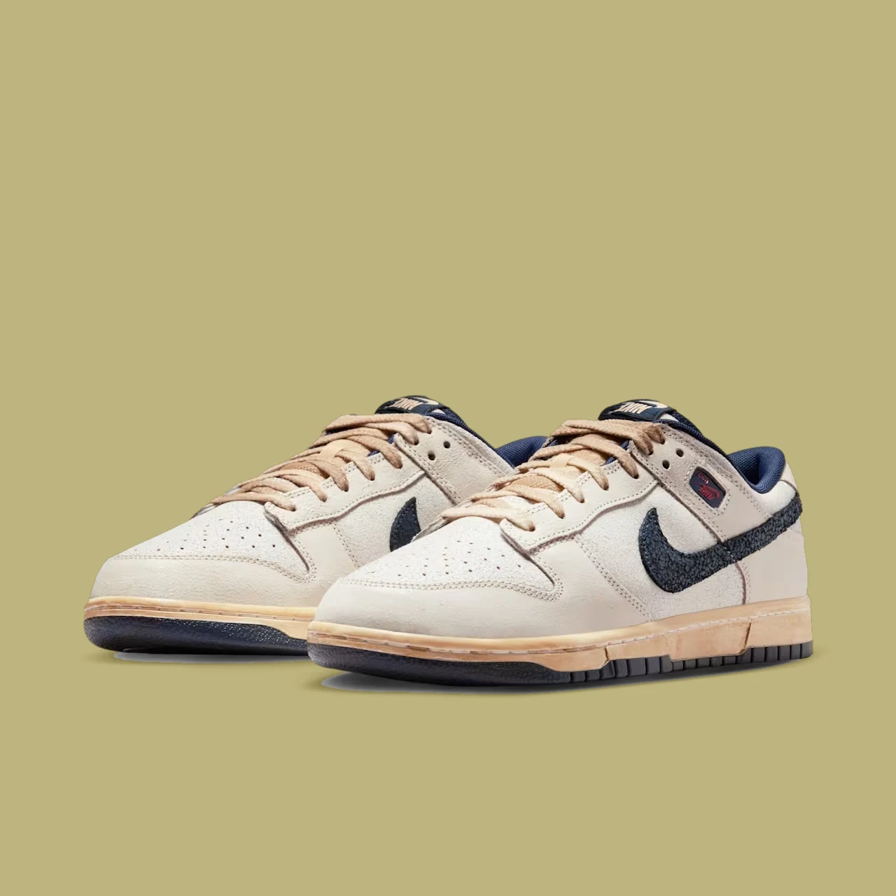 Nike Dunk Low x Stranger Things Para sportowych butów w kolorze beżowym z ciemnogranatowymi akcentami oraz charakterystycznym logo Nike po bokach, stojących na tle jednolitego, jasnobrązowego tła.
