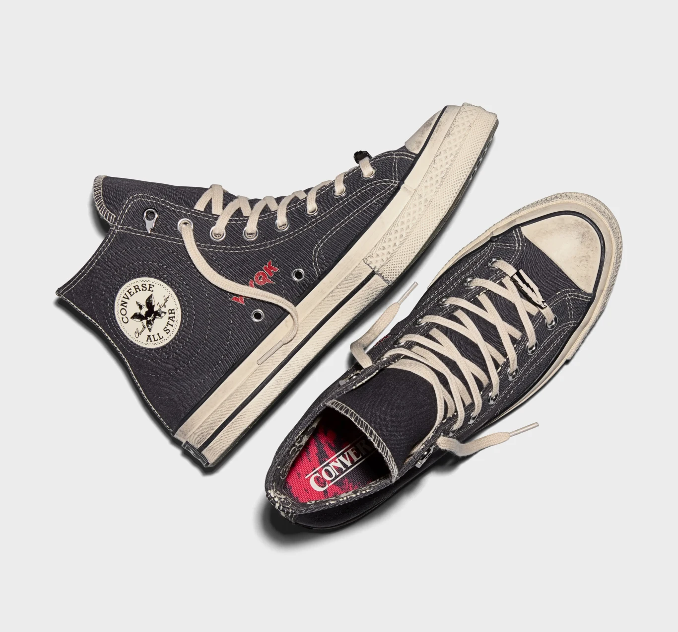 Converse Chuck 70 x Stranger Things Czarne wysokie trampki Converse All Star z kremowymi podeszwami i sznurówkami, widoczne logo marki na cholewce jednego z butów, obuwie ułożone na jasnym tle.