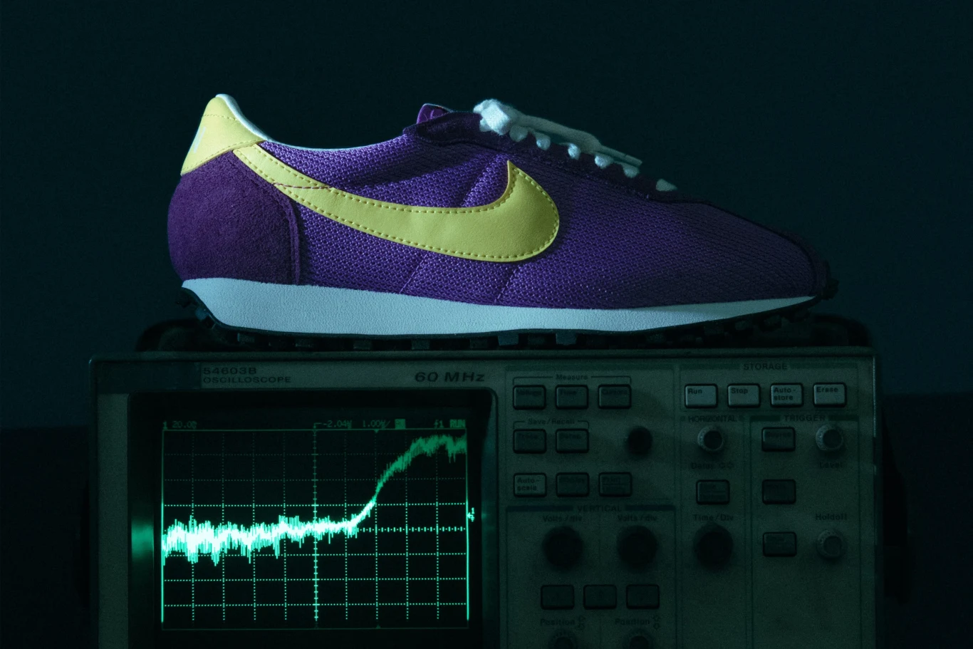 Nike x Stranger Things Fioletowo-żółty sportowy but znanej marki położony na elektronicznym oscyloskopie z wyświetlonym wykresem świetlnym na ekranie.