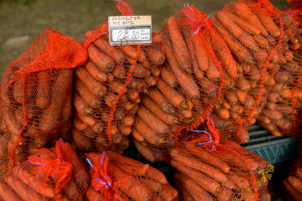 Rekordowy import marchwi do Polski Worek marchewek ułożone w czerwonych siatkach, widoczna etykieta z ceną i nazwą produktu. Warzywa ułożone są na sobie w kilku rzędach, tworząc stos.