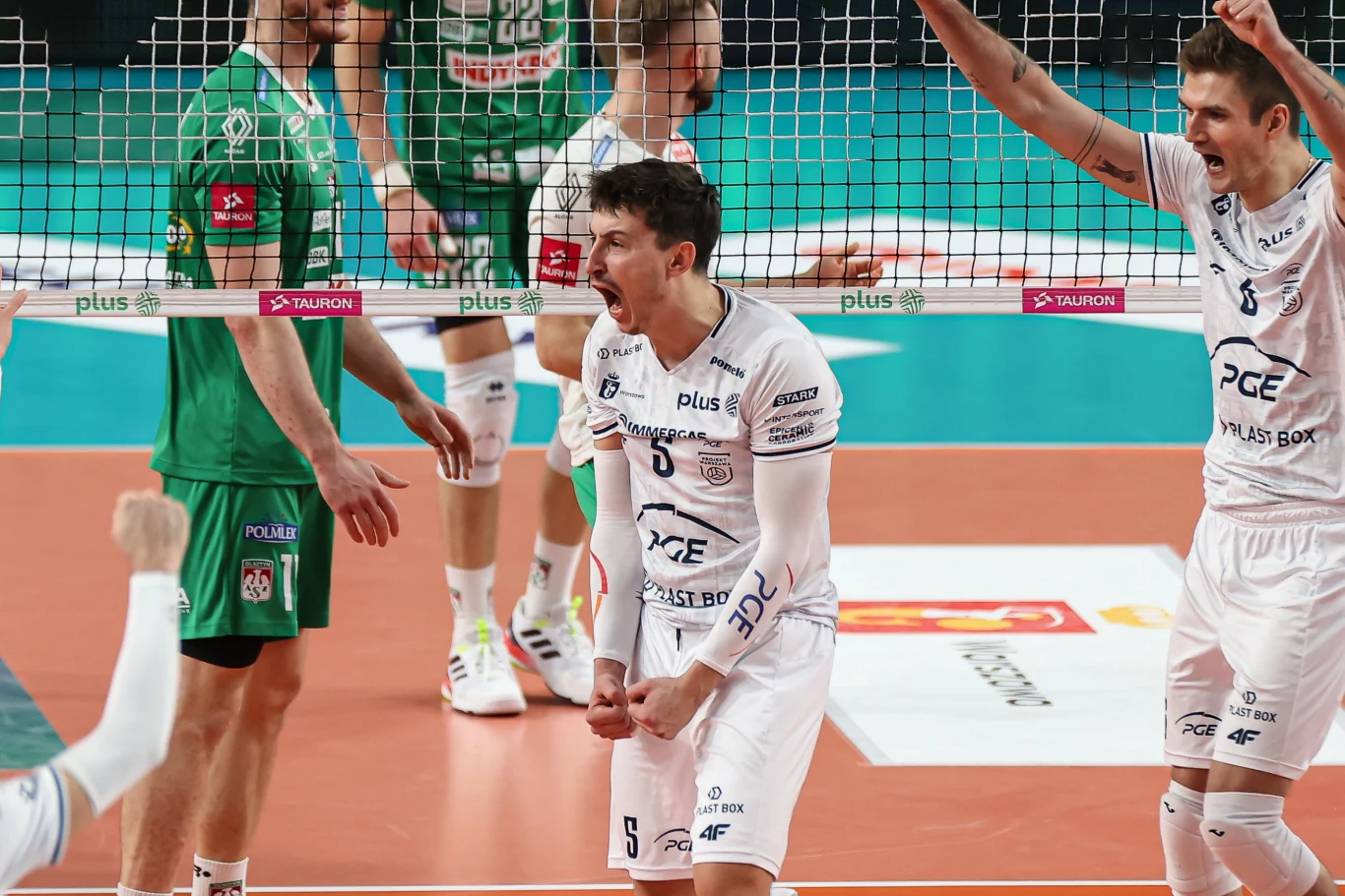 Jan Firlej Zawodnicy drużyn siatkarskich w zielonych i białych strojach po udanej akcji na boisku, z wyraźnie widoczną radością i emocjonalną reakcją sportowców.