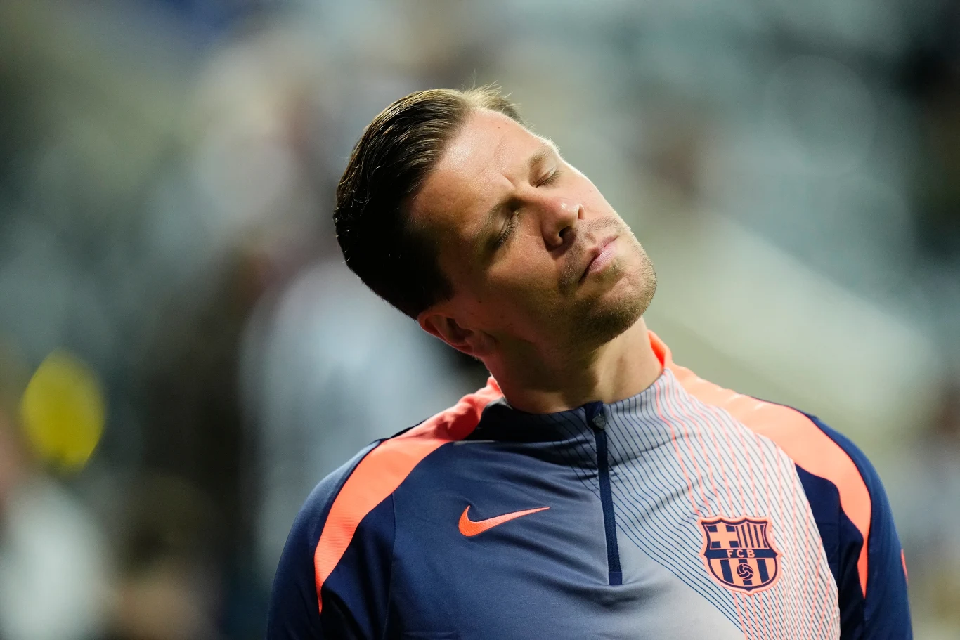 Sportowiec w stroju treningowym z herbem klubu piłkarskiego zamyka oczy i przechyla głowę w bok, sprawiając wrażenie skupienia lub zamyślenia.